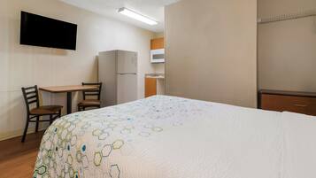 Habitación de hotel con cama, escritorio, silla, televisor, refrigerador y microondas.