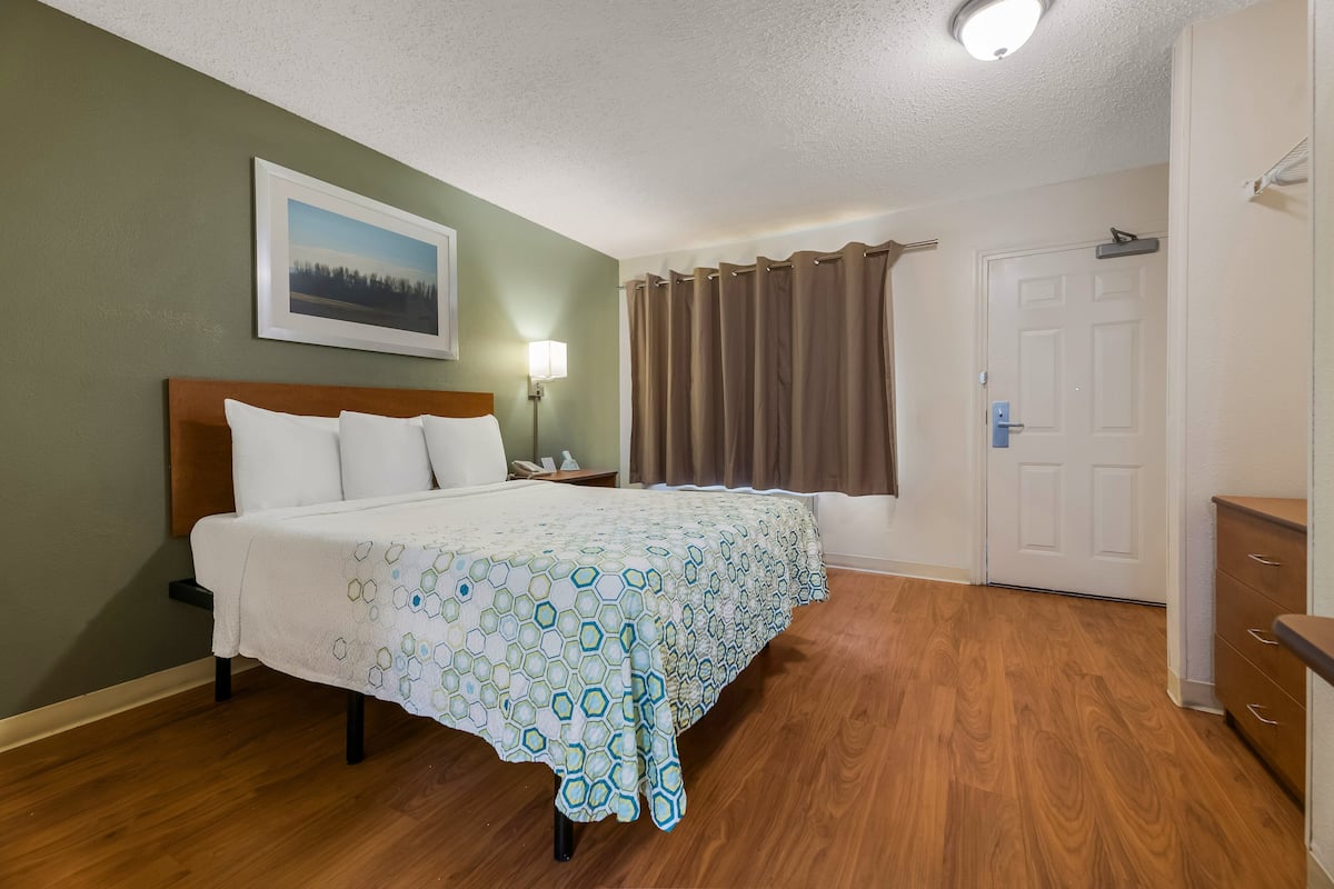 A hotel room with a bed, a nightstand, a lamp, a door, and a window with curtains.