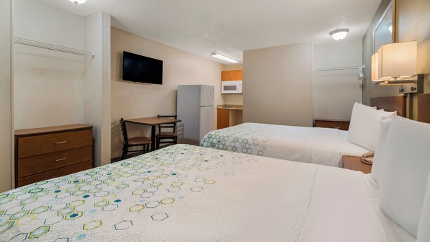 A hotel room with two beds, a desk, a chair, a television, and a microwave. - HomeTowne Studios by Red Roof Orlando - UCF Area (Orlando)
