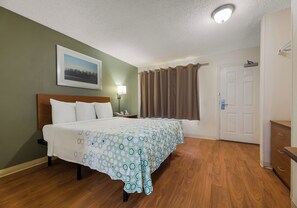 Habitación de hotel con cama, mesita de noche, lámpara, puerta y ventana con cortinas.