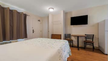 A bedroom with a bed, a desk, two chairs, a television, and a door.