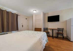 A bedroom with a bed, a desk, two chairs, a television, and a door. - HomeTowne Studios by Red Roof Orlando - UCF Area (Orlando)
