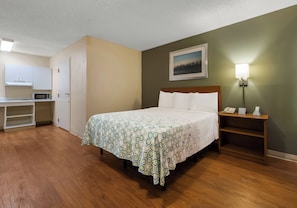 A hotel room with a bed, a desk, a microwave, a nightstand with a phone, and a picture on the wall. - HomeTowne Studios by Red Roof Orlando - UCF Area (Orlando)