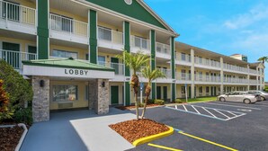 A multi-story hotel with a green and white facade, a lobby entrance, and a parking area with marked spaces. - HomeTowne Studios by Red Roof Orlando - UCF Area (Orlando)