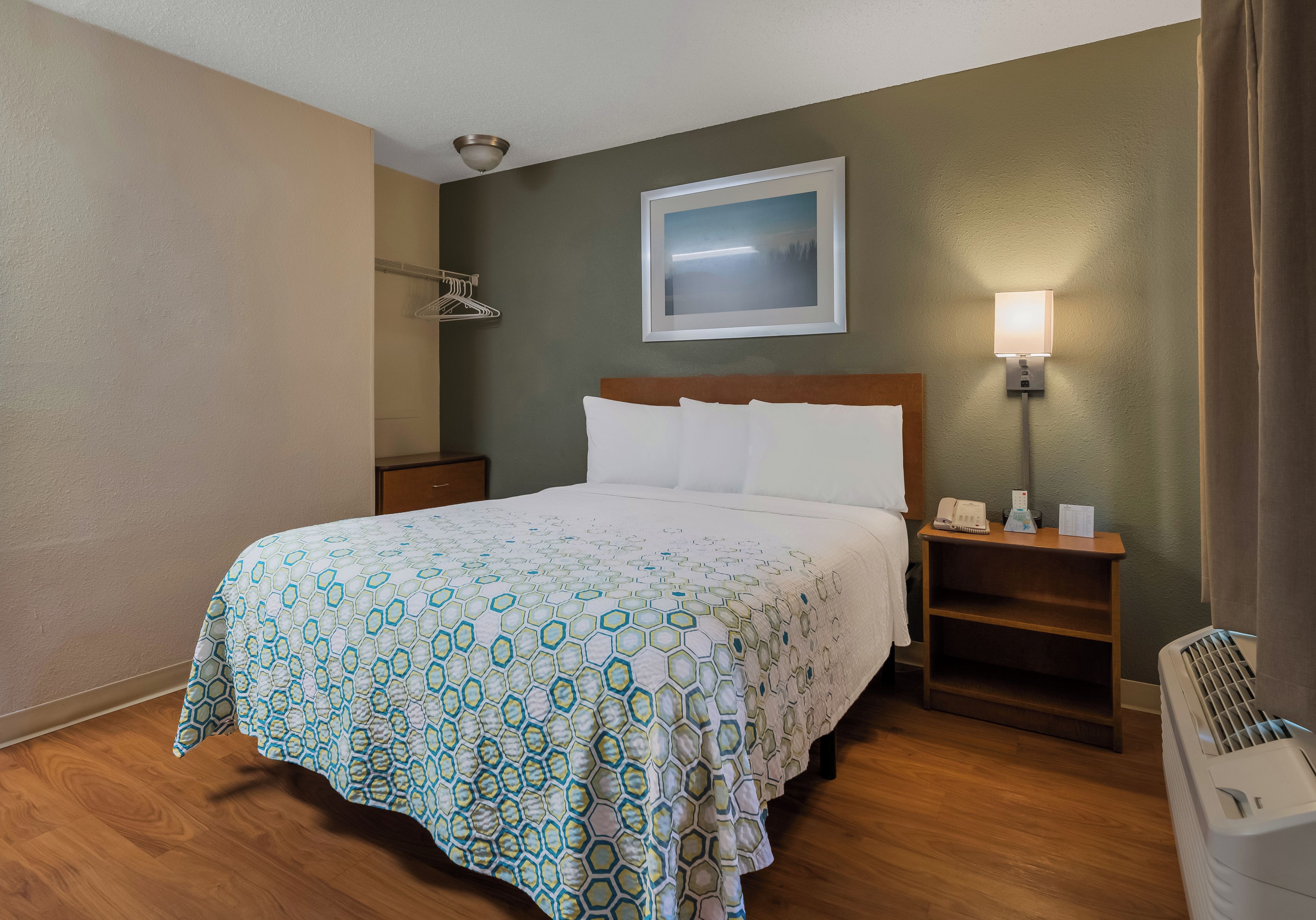 Una camera d'albergo con un letto, un comodino, una lampada e un quadro appeso al muro.
