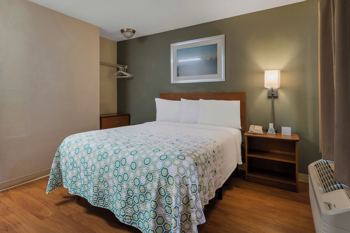 Una habitación de hotel con una cama, una mesita de noche, una lámpara y un calentador.
