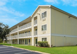 A multi-story hotel with a flat roof, balconies, and a parking lot. - HomeTowne Studios by Red Roof Orlando - UCF Area (Orlando)