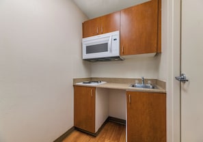 A compact kitchenette with a microwave, a sink, and wooden cabinets. - HomeTowne Studios by Red Roof Orlando - UCF Area (Orlando)