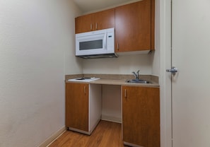 A compact kitchenette with a microwave, a sink, and wooden cabinets. - HomeTowne Studios by Red Roof Orlando - UCF Area (Orlando)