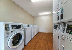 Un lavadero con varias lavadoras y secadoras, piso de madera e interior blanco.