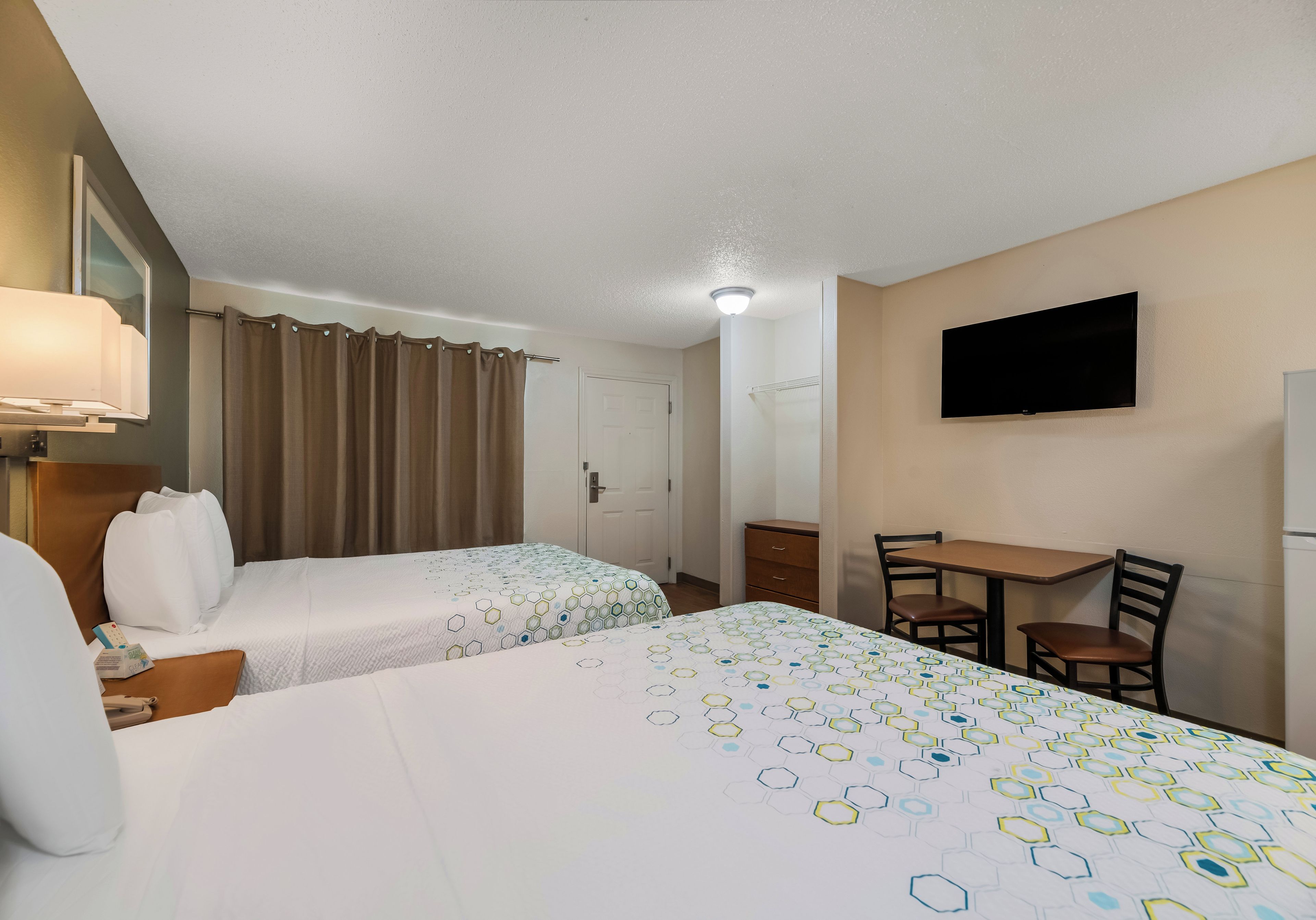 A hotel room with two beds, a desk, a chair, a television, and a bathroom door.