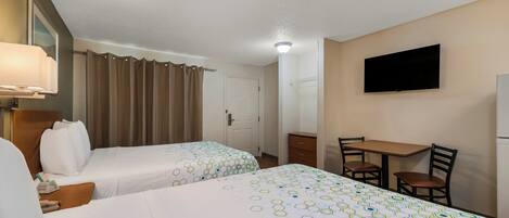 A hotel room with two beds, a desk, a chair, a television, and a bathroom door.