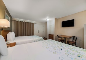 Habitación de hotel con dos camas, un escritorio, una silla, un televisor y la puerta del baño.