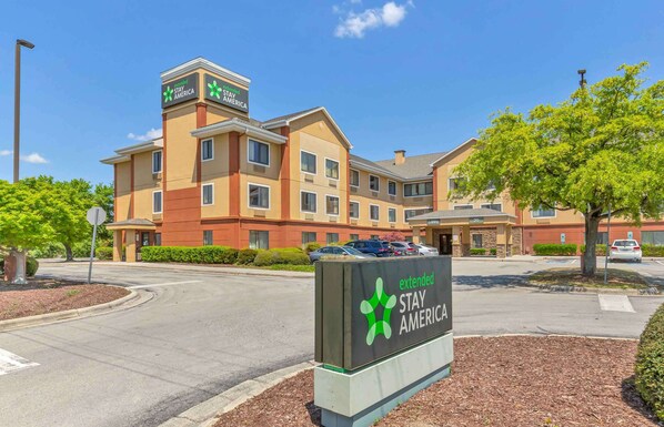 Un hotel Stay America con un letrero que indica opciones de estancia prolongada, un estacionamiento y un cielo azul despejado.