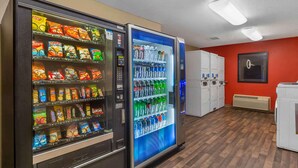 Two vending machines with snacks and bottled water in a room with wooden flooring and a red wall. - Extended Stay America Suites Jacksonville Camp Lejeune (Jacksonville)
