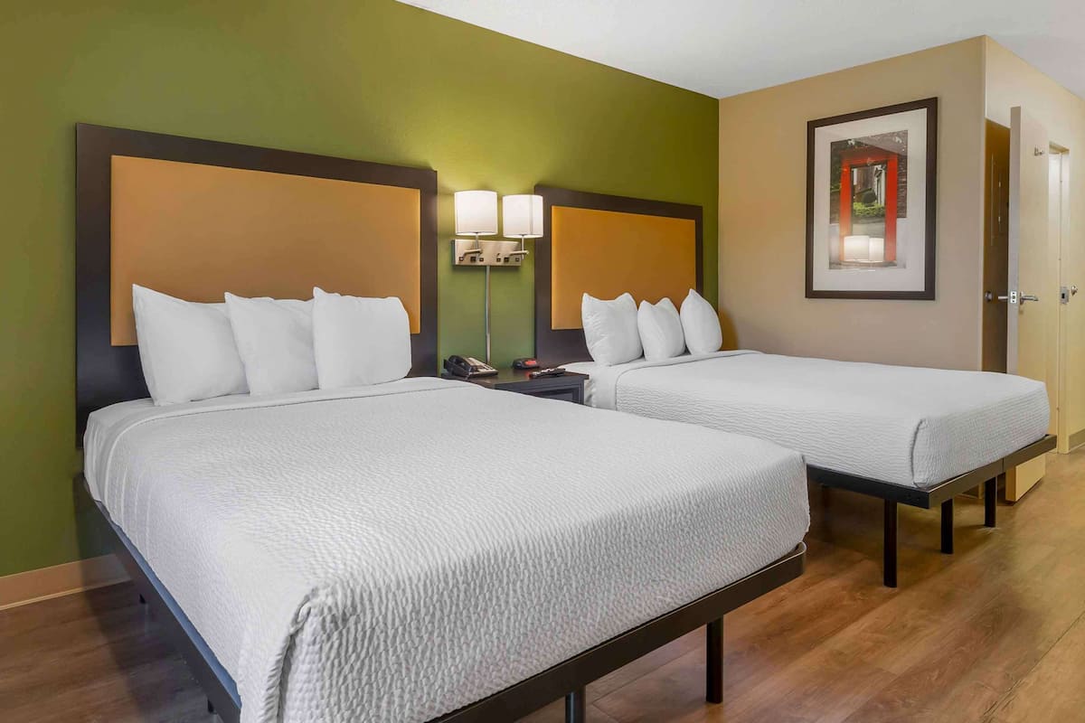 A hotel room with two beds, a nightstand with a lamp, and a framed picture on the wall.