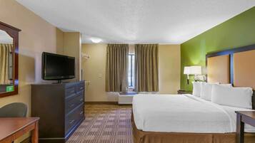 A hotel room with a bed, a TV on a dresser, a desk, and a window with curtains.