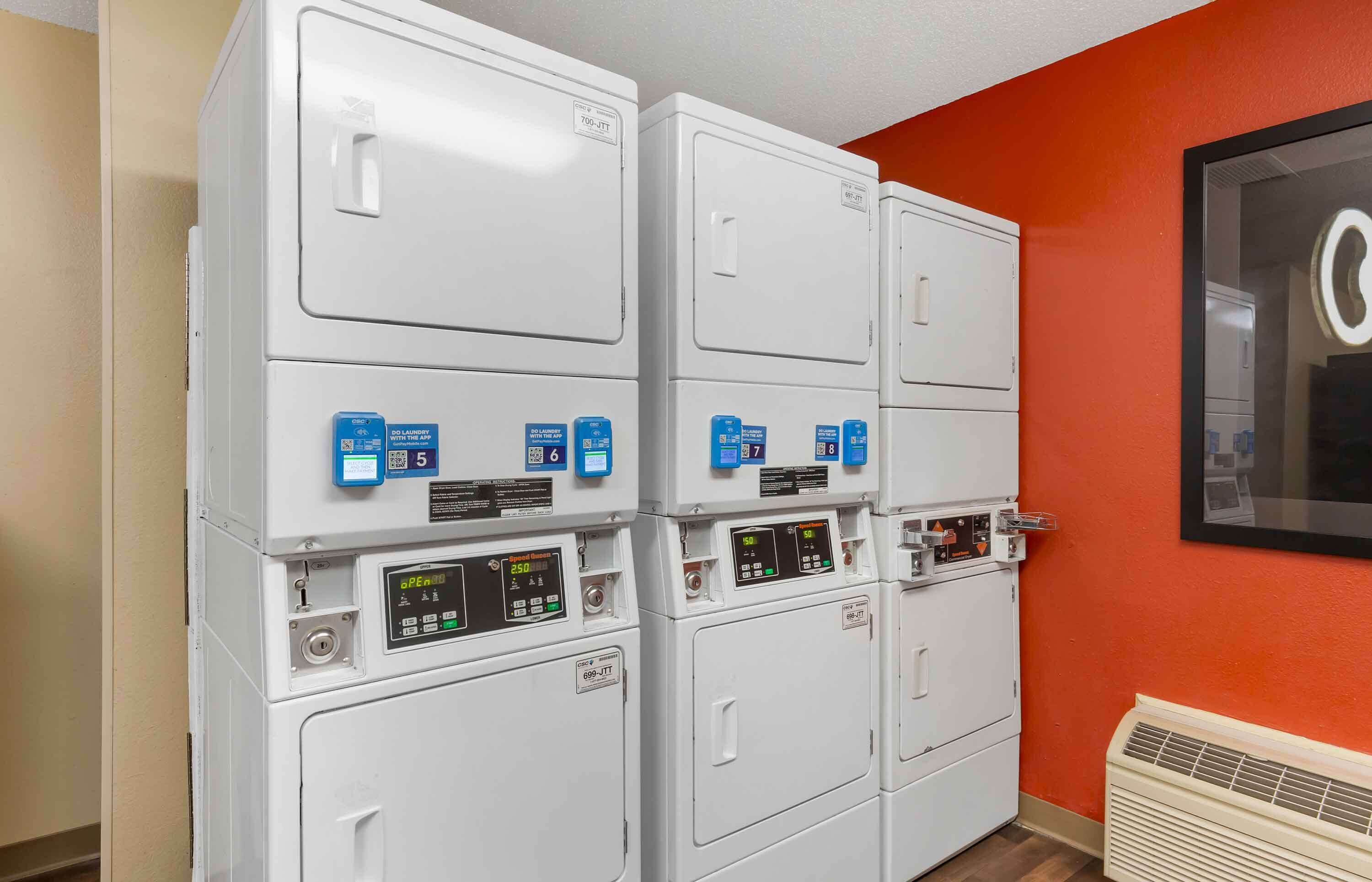 A laundry area with four stacked washers and dryers, each with control panels and digital displays.