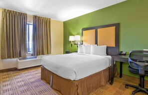 A hotel room with a large bed, a desk with a chair, a window with curtains, and a wall-mounted lamp. - Extended Stay America Suites Jacksonville Camp Lejeune (Jacksonville)