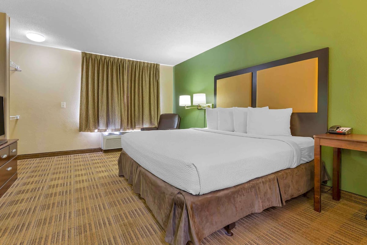 A hotel room with a large bed, a desk, a chair, a television, and a window with curtains.