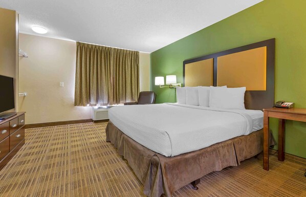A hotel room with a large bed, a desk, a chair, a television, and a window with curtains.