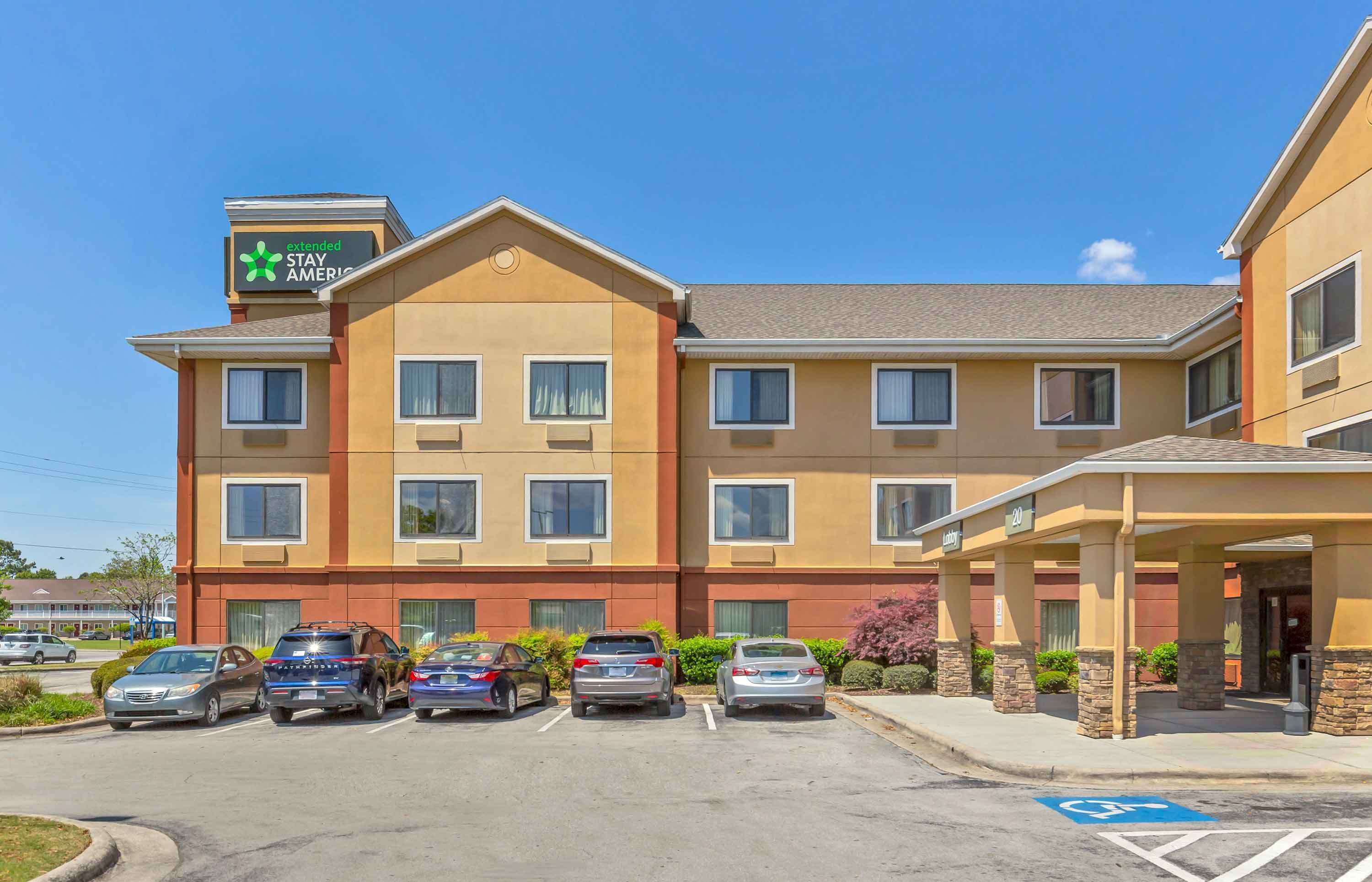Un hôtel à plusieurs étages, avec une enseigne indiquant « Extended Stay America » et un parking où sont garées plusieurs voitures.