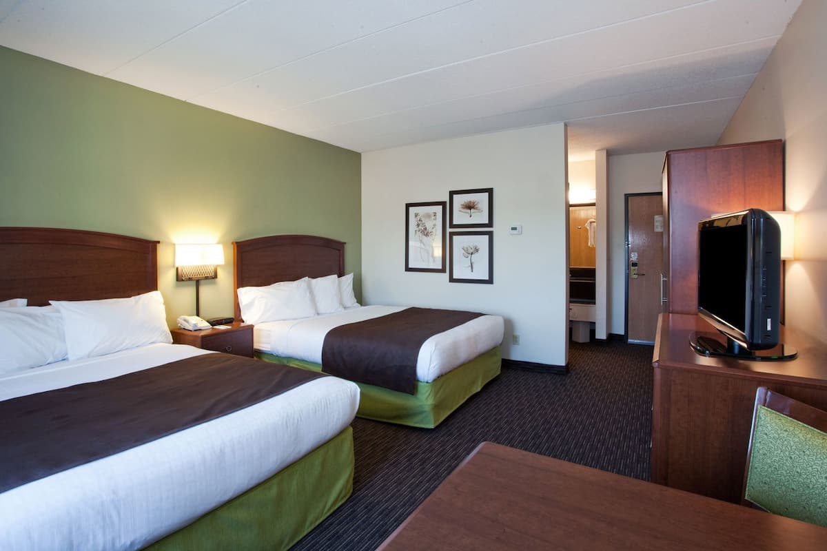 A hotel room with two beds, a TV, a desk, and a bathroom visible through an open door.