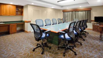 A conference room with a long table, six chairs, a television, and a kitchenette area.