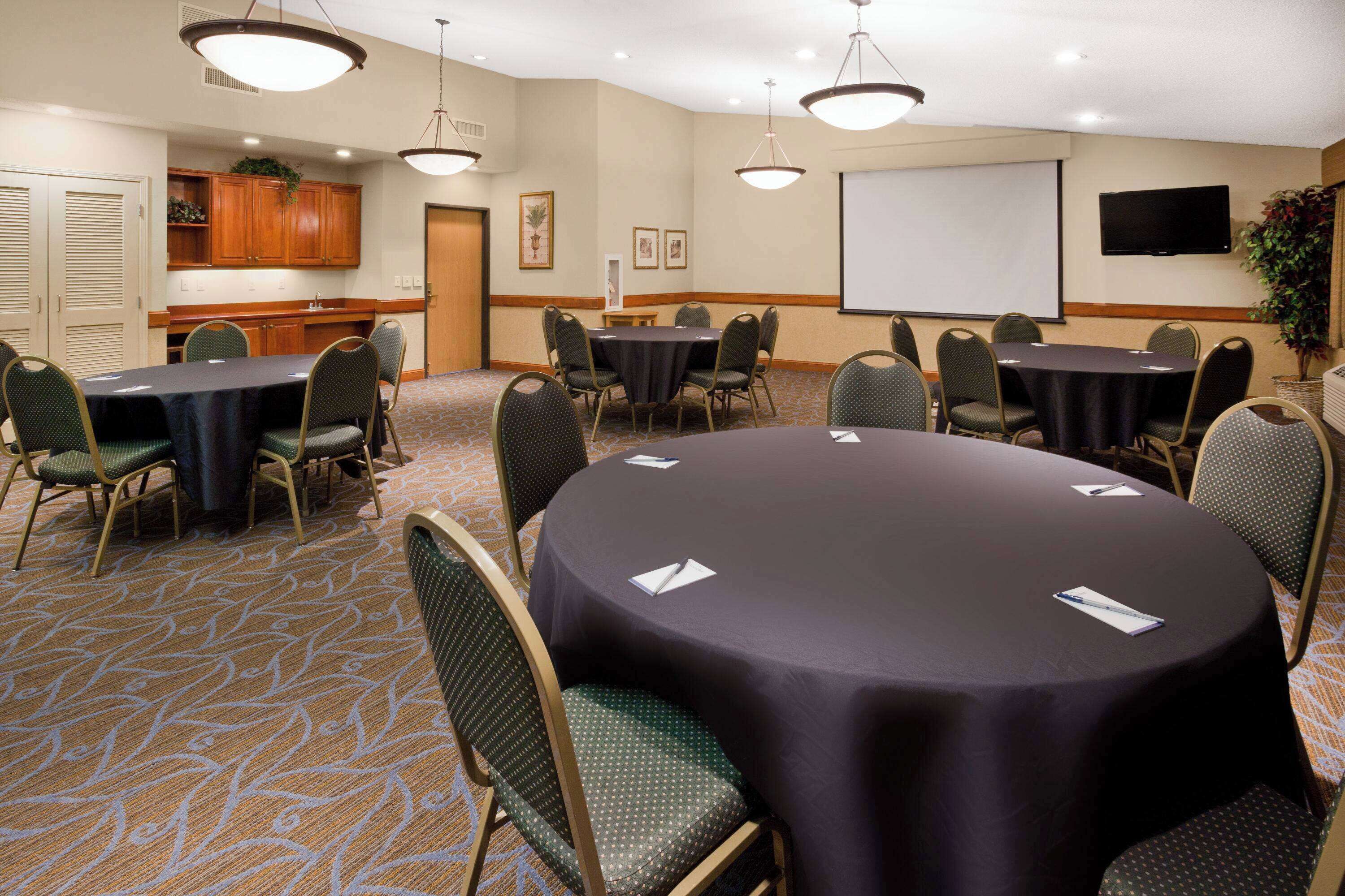 A conference room with round tables, chairs, a projector screen, and a television.