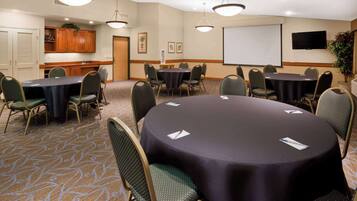 A conference room with round tables, chairs, a projector screen, and a television.