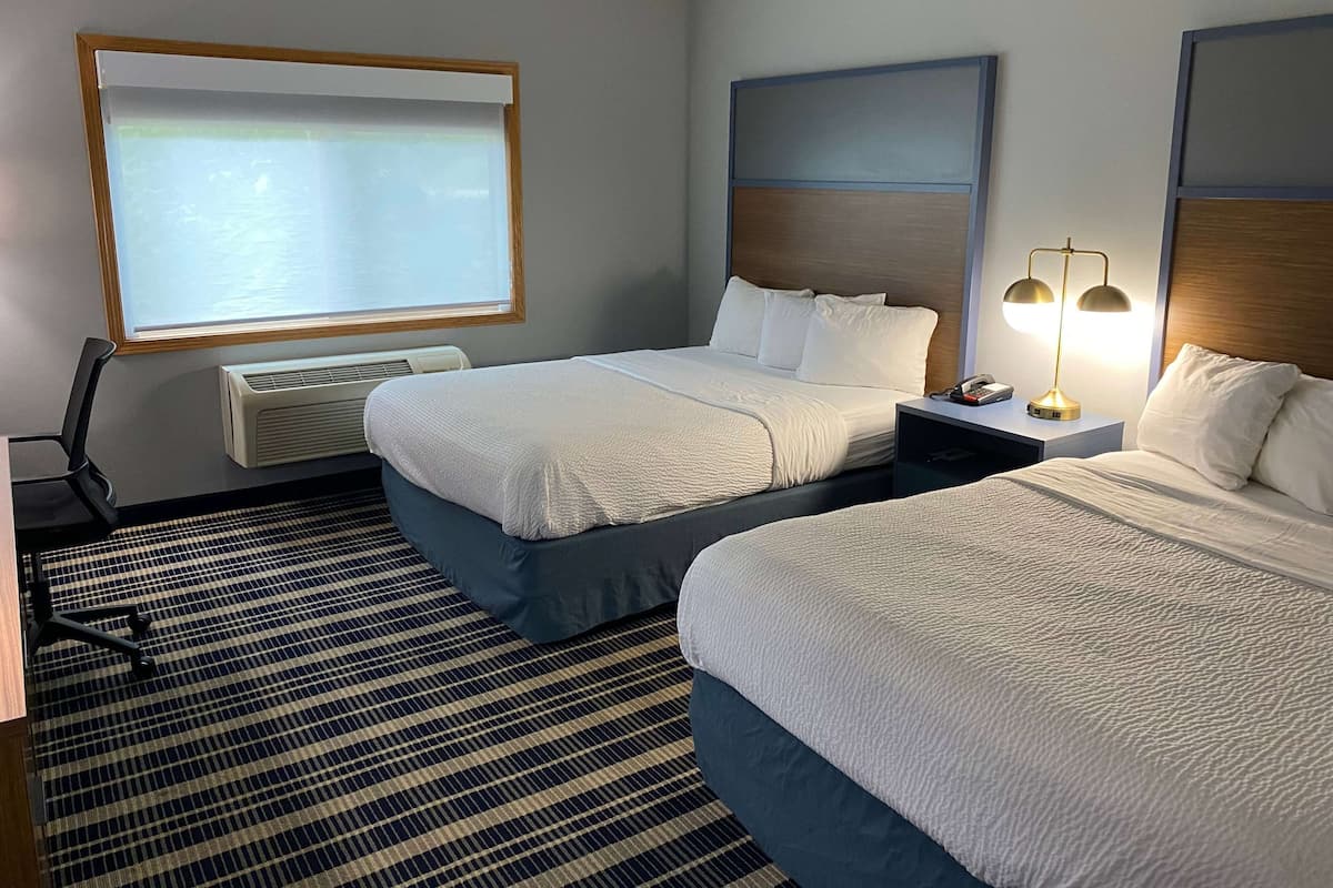 Ein Hotelzimmer mit zwei Betten, einem Schreibtisch, einem Stuhl, einer Projektionsleinwand und einer Lampe.