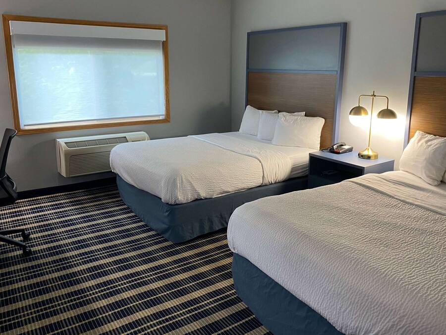 A hotel room with two beds, a desk, a chair, a projector screen, and a lamp.