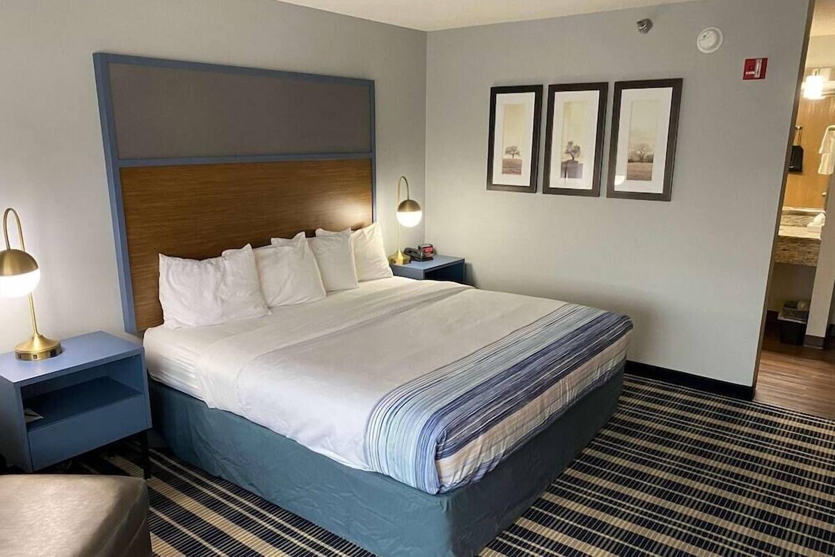 Ein Hotelzimmer mit einem großen Bett, einem Nachttisch mit Lampe und einer Wand mit drei gerahmten Bildern.