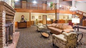 A spacious lobby with a fireplace, a leather sofa, and a patterned carpet. - AmericInn by Wyndham Chanhassen (Chanhassen)