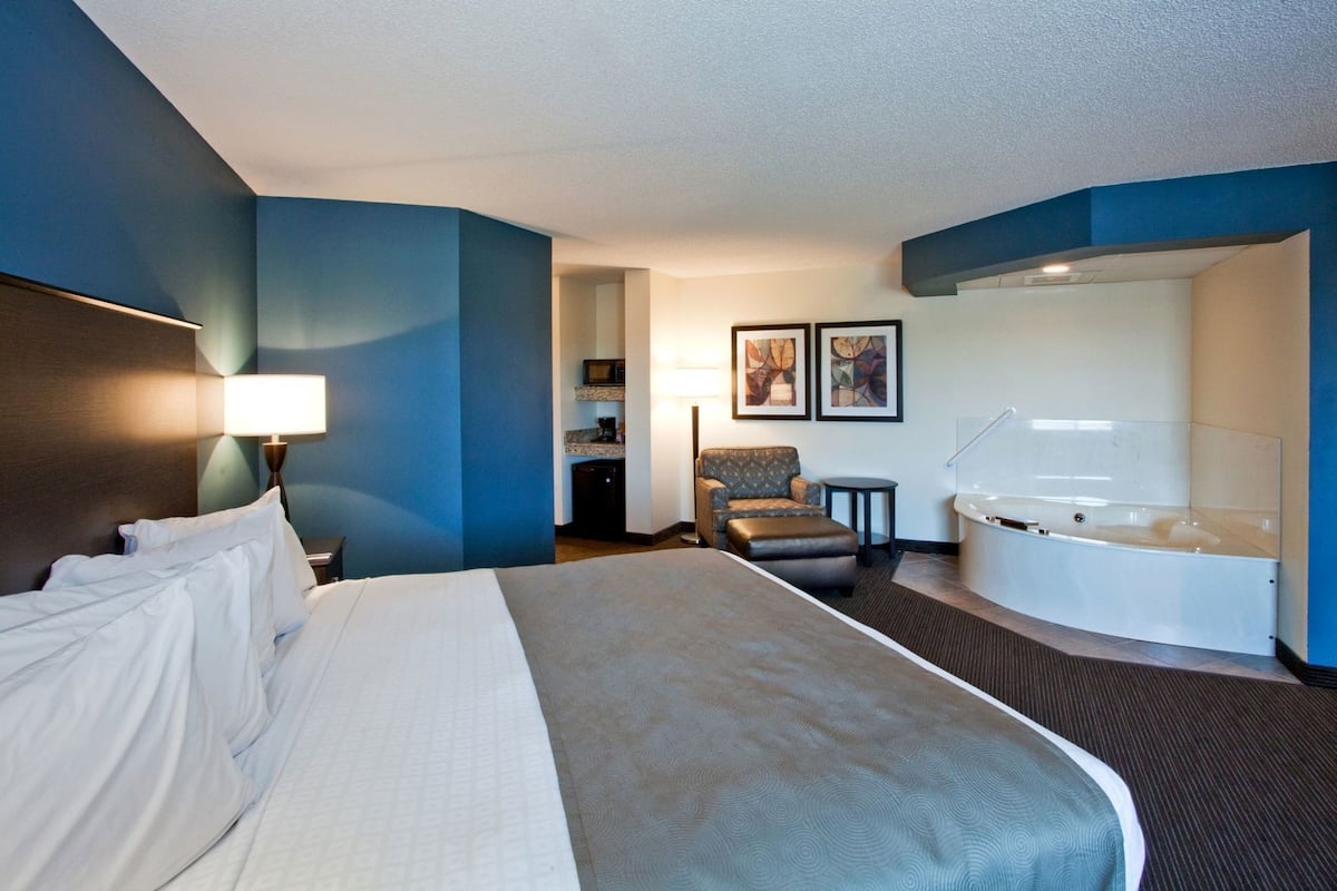 Ein Hotelzimmer mit Bett, Sessel, kleinem Tisch, Badewanne und einer Mikrowelle in der Ecke.