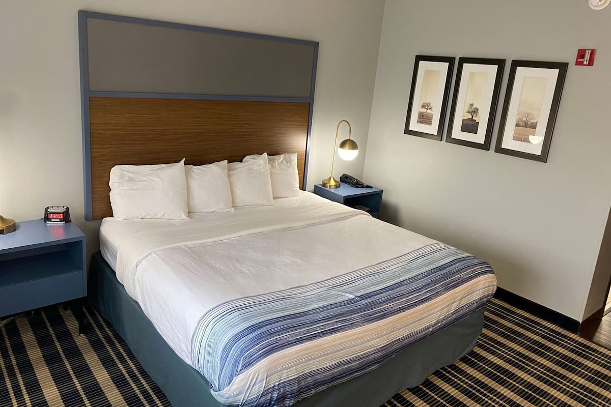 Ein Hotelzimmer mit einem großen Bett, einem Nachttisch mit Lampe und drei gerahmten Bildern an der Wand.