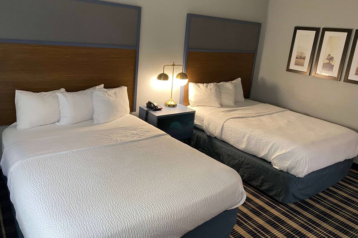 Ein Hotelzimmer mit zwei Betten, einem Nachttisch mit Lampe und gerahmten Bildern an der Wand.