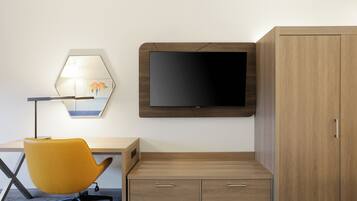 Una habitación de hotel moderna con un escritorio de madera, una silla amarilla, un televisor de pantalla plana y un armario.