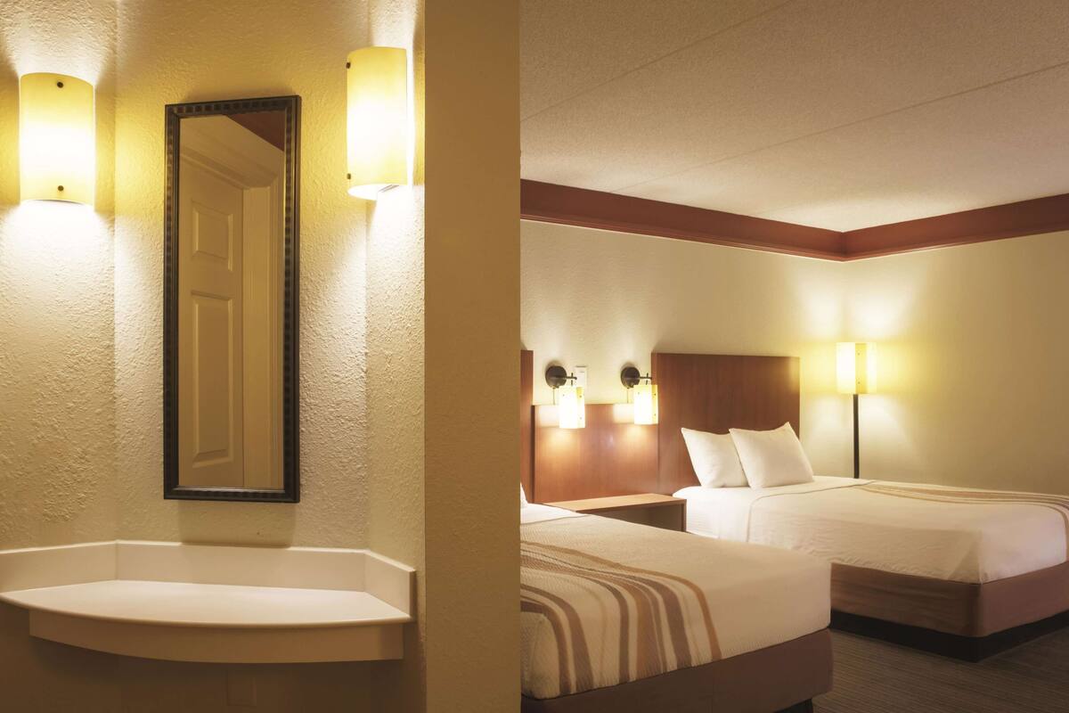 A hotel room with a large mirror, two bedside lamps, a bed with a striped bedspread, and a nightstand.