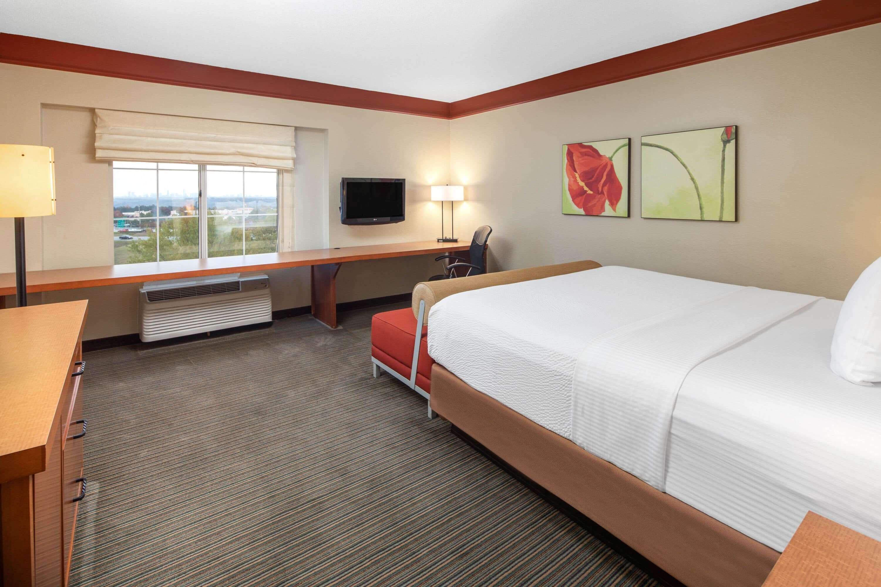 A hotel room with a large bed, a desk, a chair, a TV, and a window with a view.