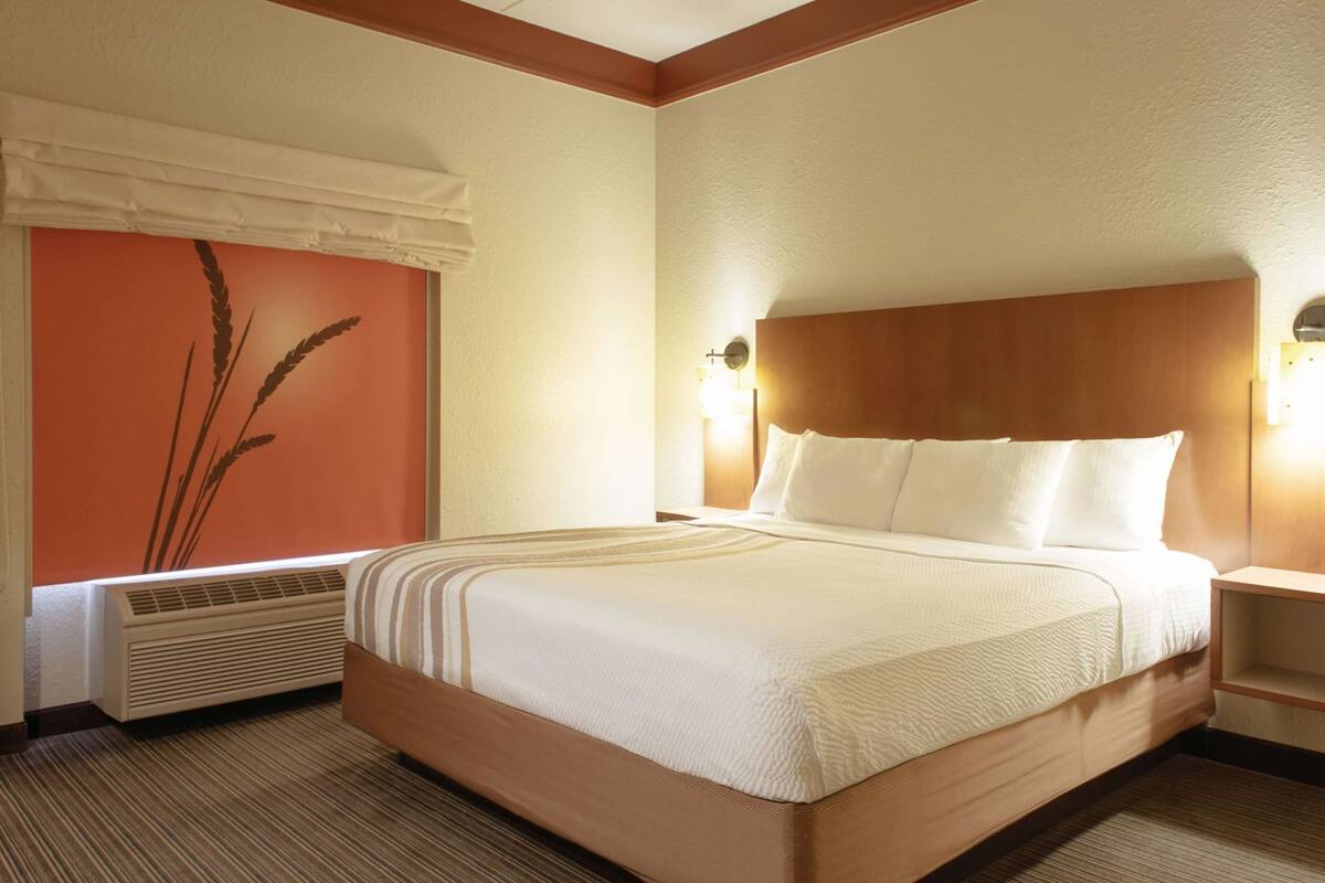 A hotel room with a large bed, a wall-mounted air conditioner, and a decorative wall panel.