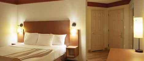 Quarto de hotel com uma cama grande, abajures, cabeceira de madeira e uma porta que dá para outro cômodo.