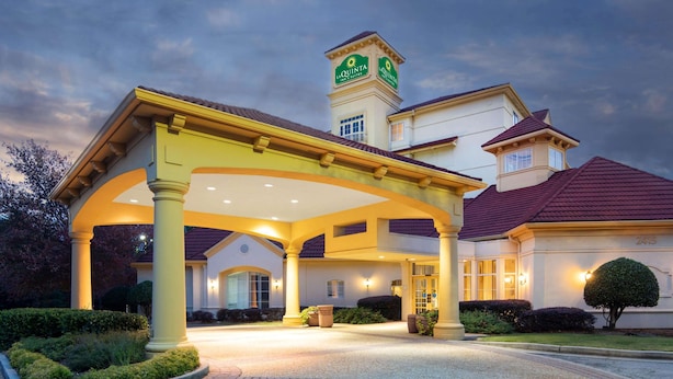 A hotel entrance with a covered patio, a tower with signage, and well-maintained landscaping.