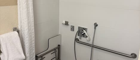 A wheelchair-accessible shower area with a grab bar, a towel rack, and a bench.