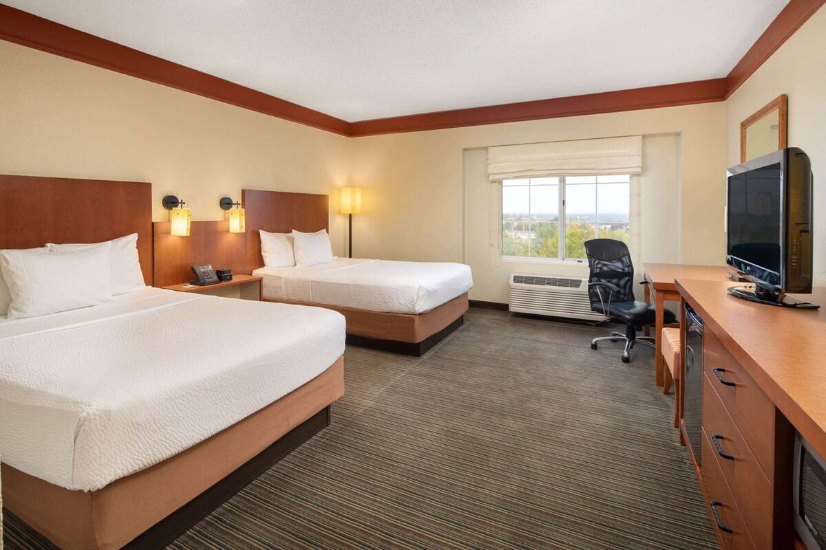 A hotel room with two beds, a desk, a chair, a television, and a window with a view.