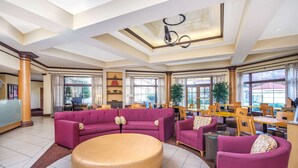 A spacious lobby with a large round table, purple sofas, and a dining area with wooden tables and chairs.