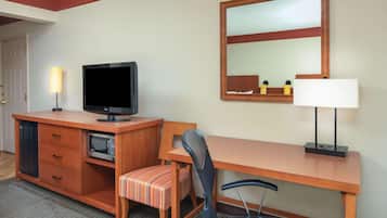 A hotel room with a wooden desk, a television, a microwave, a chair, a lamp, and a mirror.