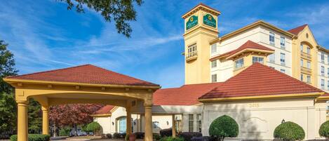 A hotel with a red-tiled roof, a central tower with a clock, and a covered entrance area.