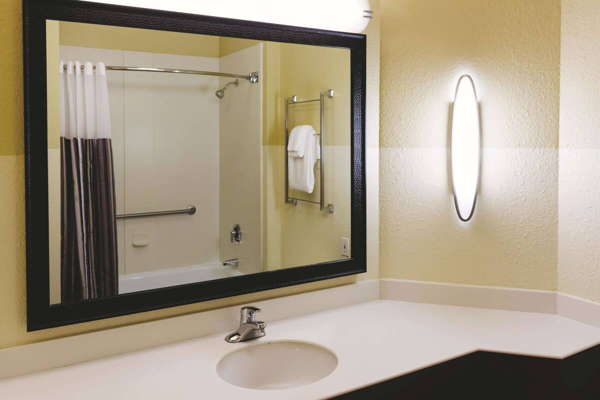 A bathroom with a large mirror, a sink, and a towel rack.