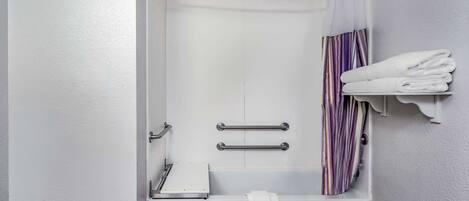 A bathroom with a bathtub, a shower curtain, a towel rack, and a shelf with folded towels.